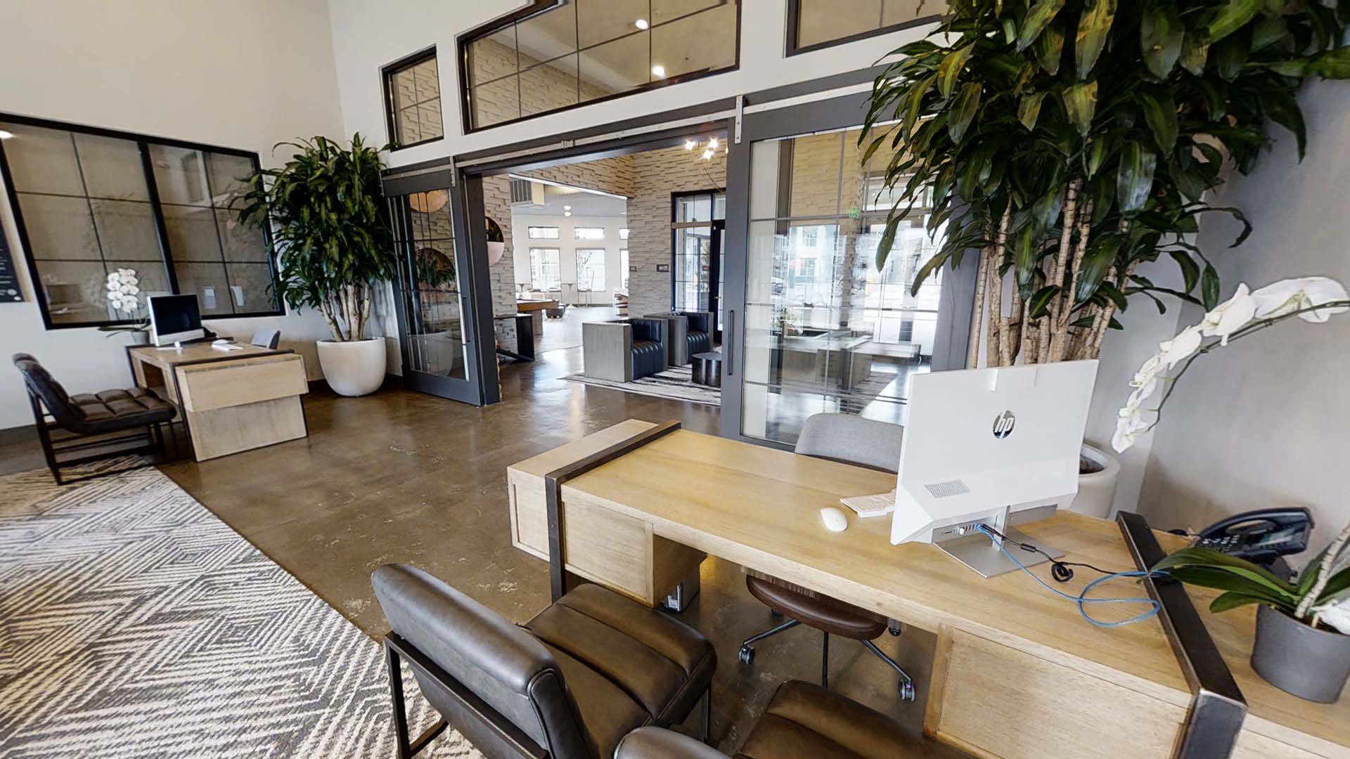 Clubhouse with leasing desks, computers, and large potted plants.